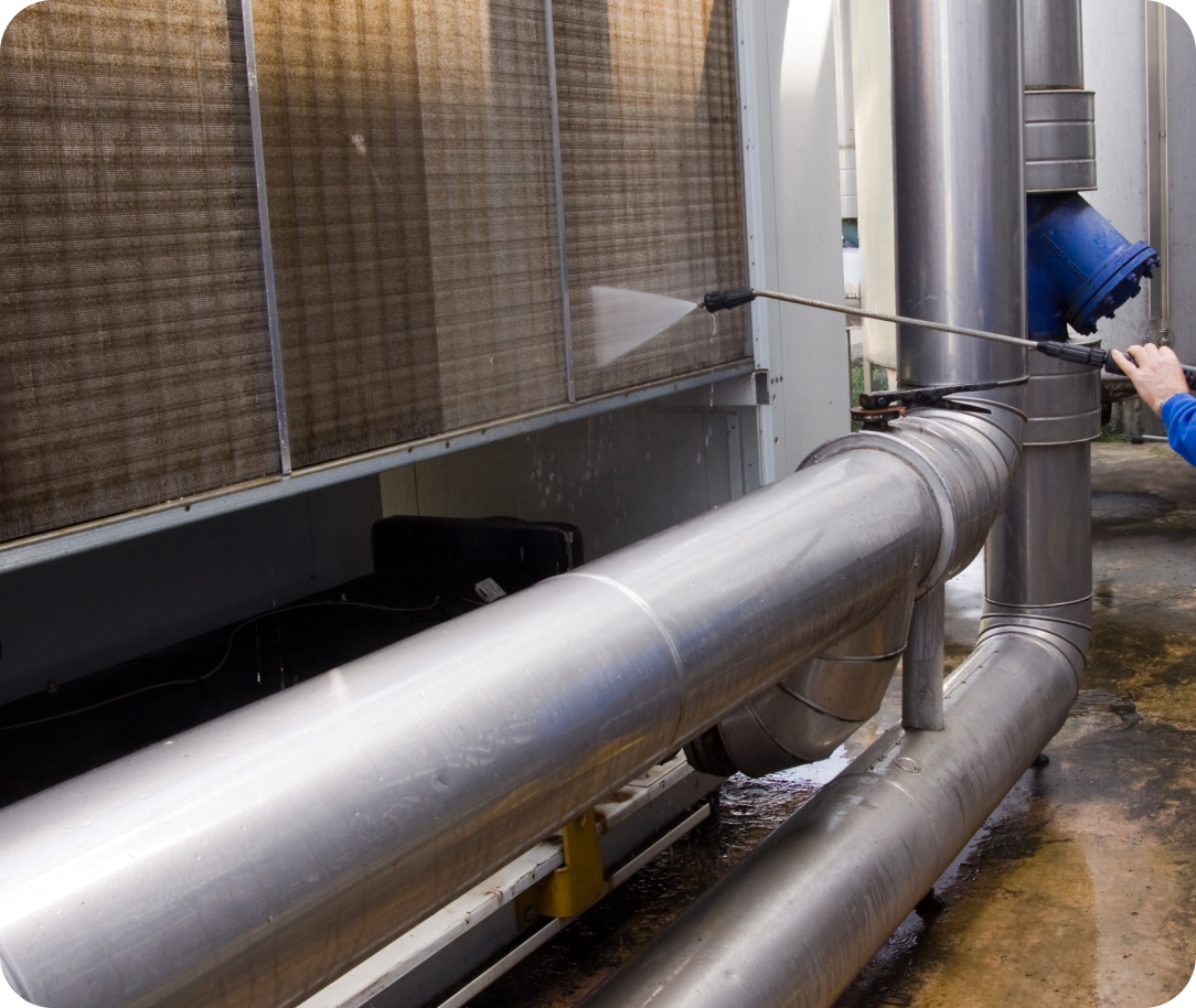 Industrial pipes being cleaned with a pressure washer, showcasing a worker handling the nozzle for maintenance cleaning.